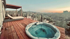 Terraza de madera con jacuzzi y sillones de descanso con vistas a un paisaje pintoresco.
