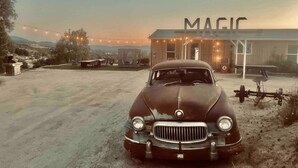 Un coche antiguo estacionado frente a un edificio con la leyenda 'MAGIC'.