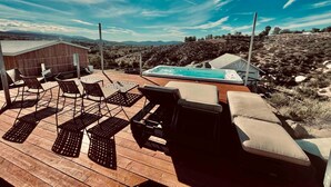 Una terraza de madera con mobiliario exterior, un jacuzzi y vistas a un paisaje montañoso.