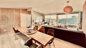 A modern dining area with a wooden table and chairs, a large window with a view of the outdoors, and a hexagonal pendant light. - Mountain View Ranch Pool Hot Tub 15guests (Temecula)