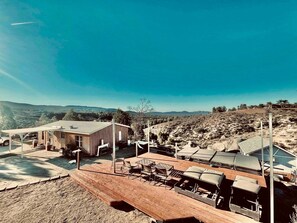 A modern building with a wooden deck and outdoor seating area, surrounded by a hilly landscape. - Mountain View Ranch Pool Hot Tub 15guests (Temecula)