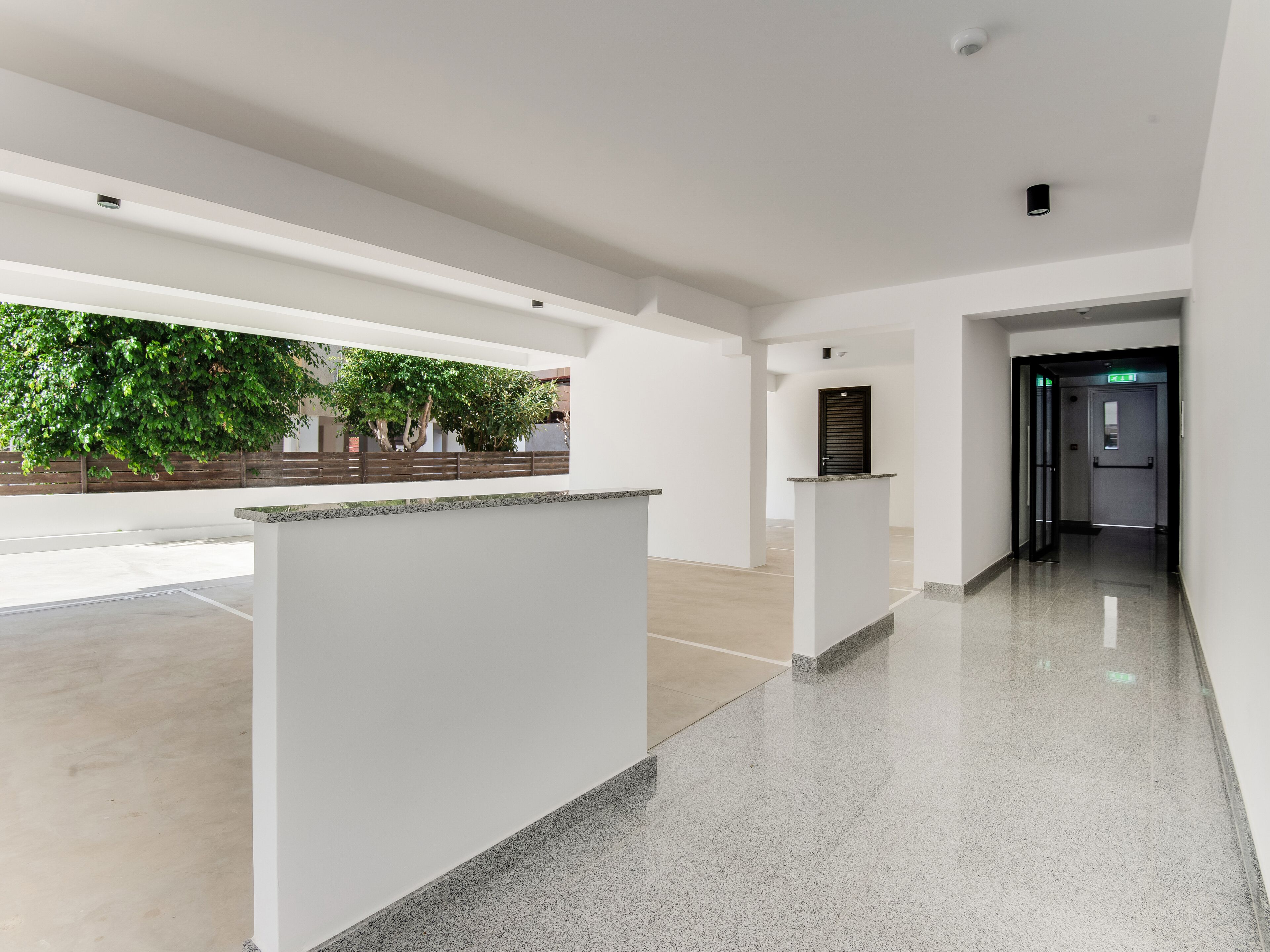 A modern hotel lobby with a reception desk, a glass door leading to the elevator, and a view of the outdoors.