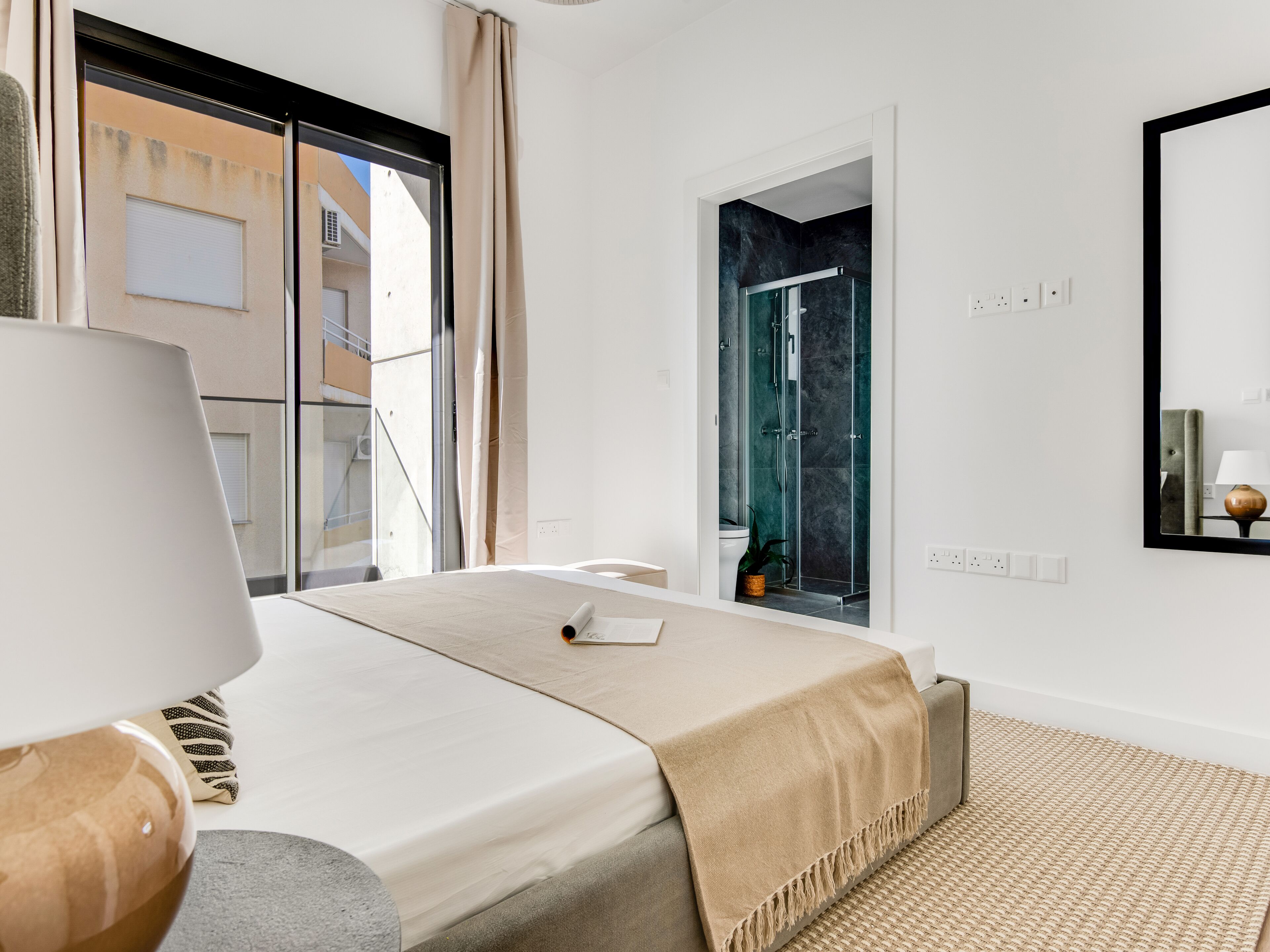 Une chambre d’hôtel moderne, équipée d’un lit, d’une table de chevet, d’une lampe, d’une douche et offrant une vue sur l’extérieur.