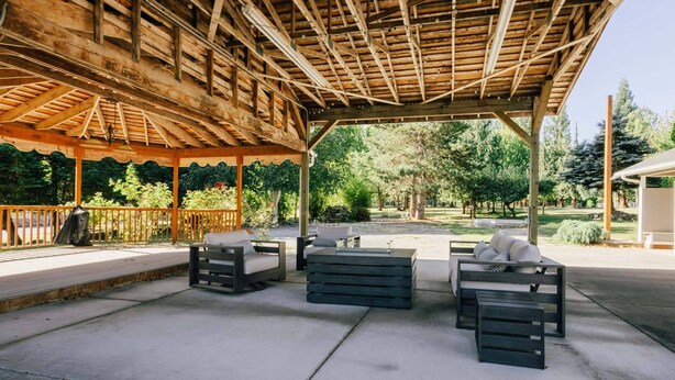 Un patio al aire libre con vigas de madera, piso de concreto y arreglos de mobiliario.