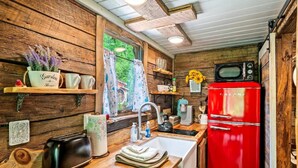 Una cocina rústica con paredes de madera, un refrigerador rojo, una tetera, una cafetera y una ventana con cortinas.