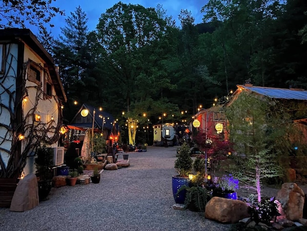 A rustic outdoor setting with a gravel path, wooden structures, and string lights.