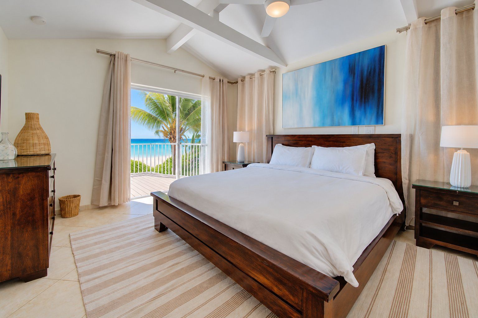 A hotel room with a large bed, a painting, a view of the ocean, and a balcony.