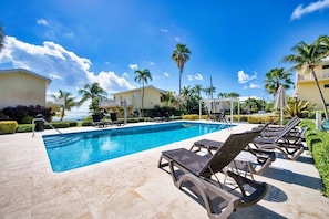 A pool area with lounge chairs, palm trees, and a clear sky.