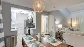 Ein modernes Wohnzimmer mit Essbereich, grauen Wänden und einer durchgehenden Tür sichtbaren Küche.