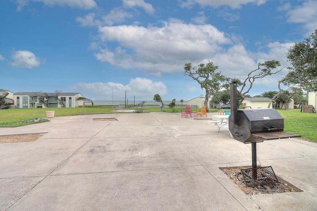 A spacious outdoor patio with a barbecue grill, picnic tables, and a grassy area.