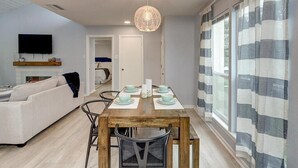 Ein modernes Wohnzimmer mit einer Couch, einem Esstisch für vier Personen und einem an der Wand befestigten Fernseher.