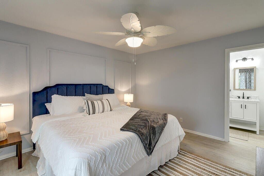 A bedroom with a bed, a nightstand, a ceiling fan, and a bathroom visible through an open door.