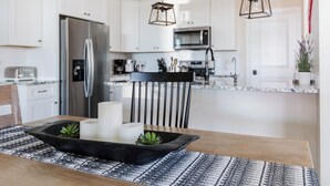 Cuina moderna amb armaris blancs, electrodomèstics d'acer inoxidable i una cadira negra.