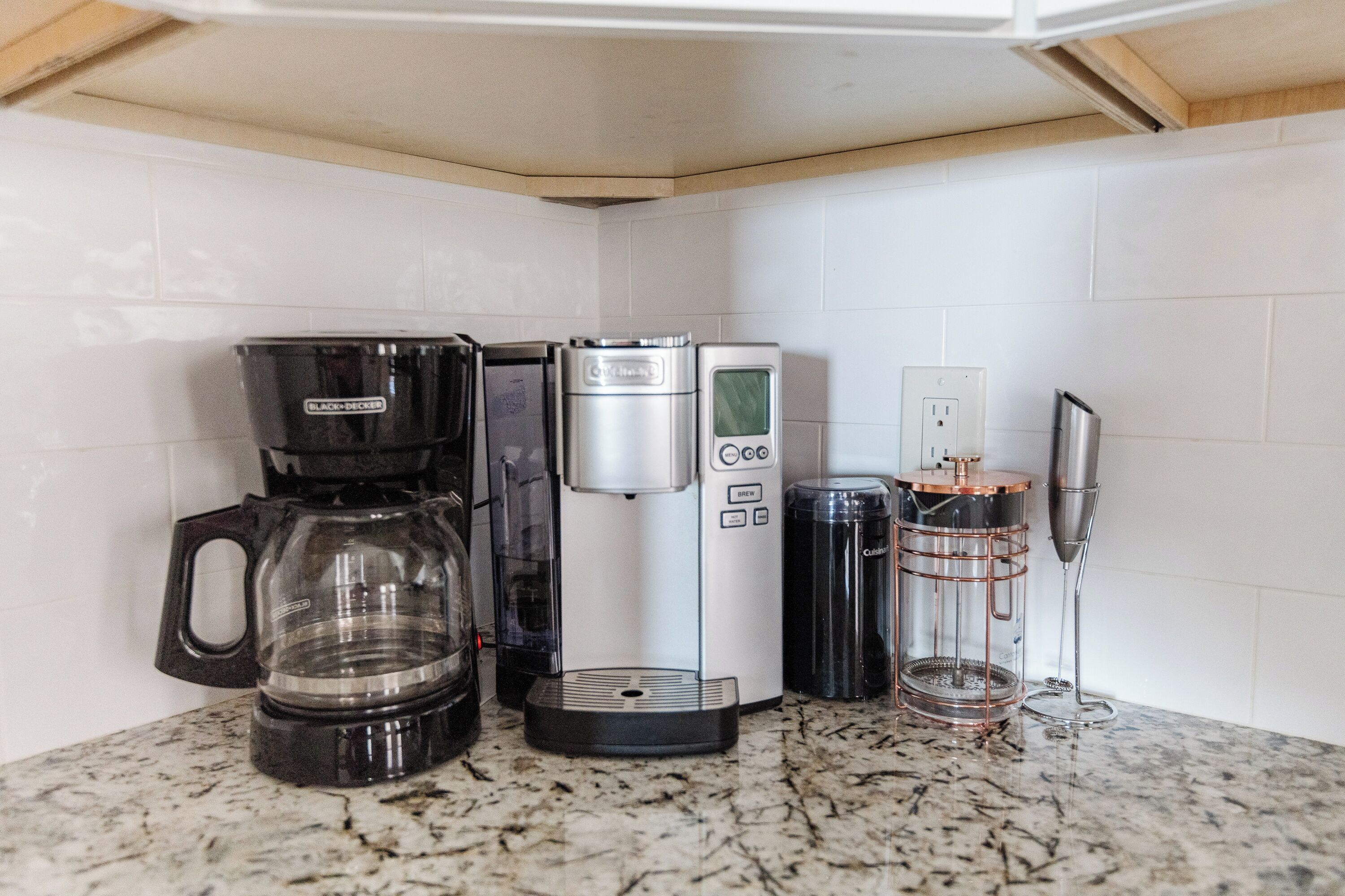 A kitchen with a coffee maker, a kettle, and a coffee pot on a granite countertop.