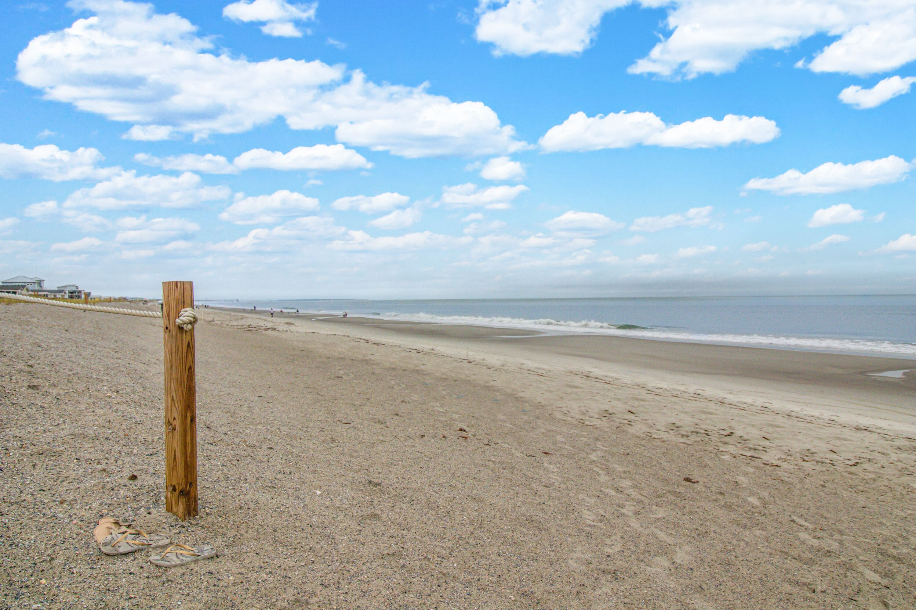 A beach with a wooden post and a pair of sandals on the sand.