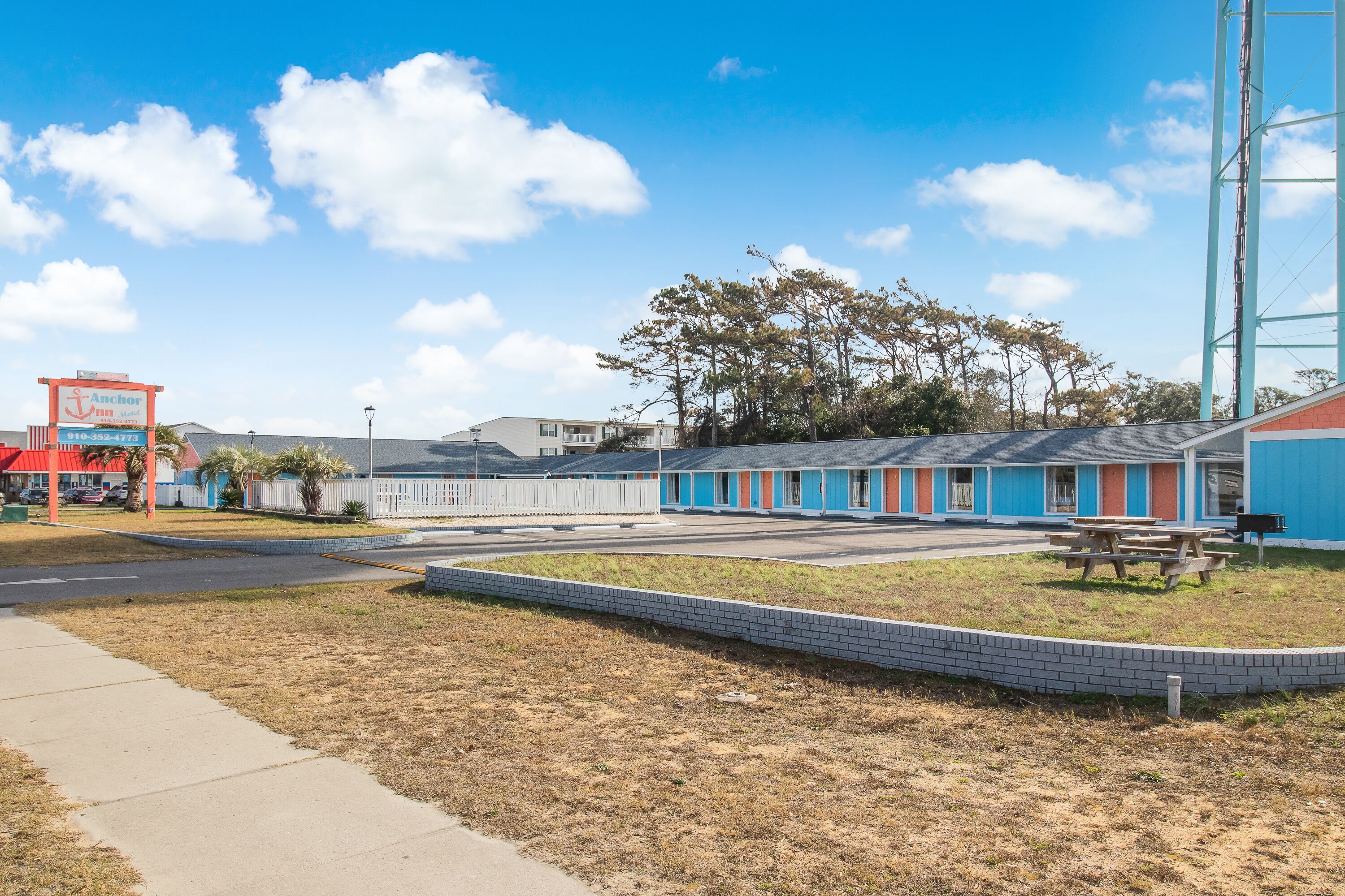 Een motel met kleurrijke buitenmuren, een parkeerplaats en een gazon met picknicktafels.