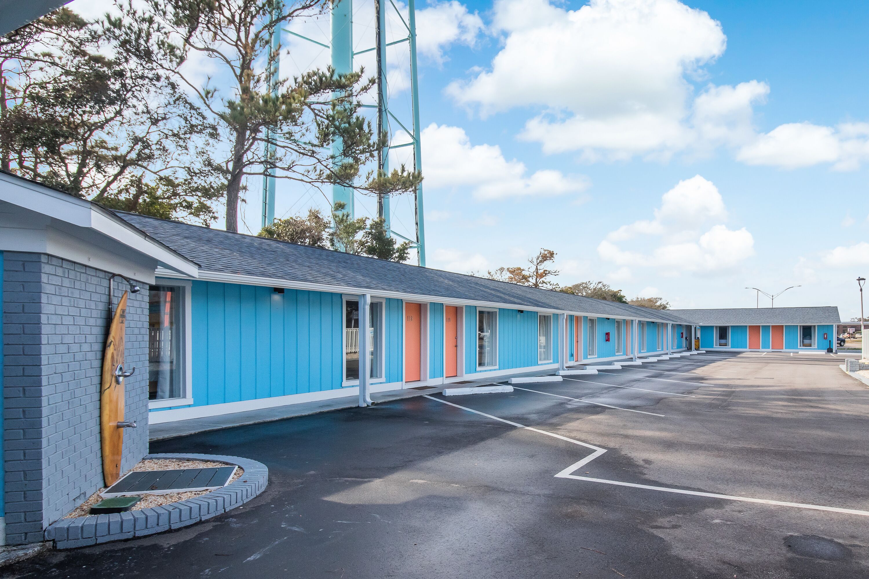A motel with a row of rooms, each with a different colored door, and a parking lot in front.