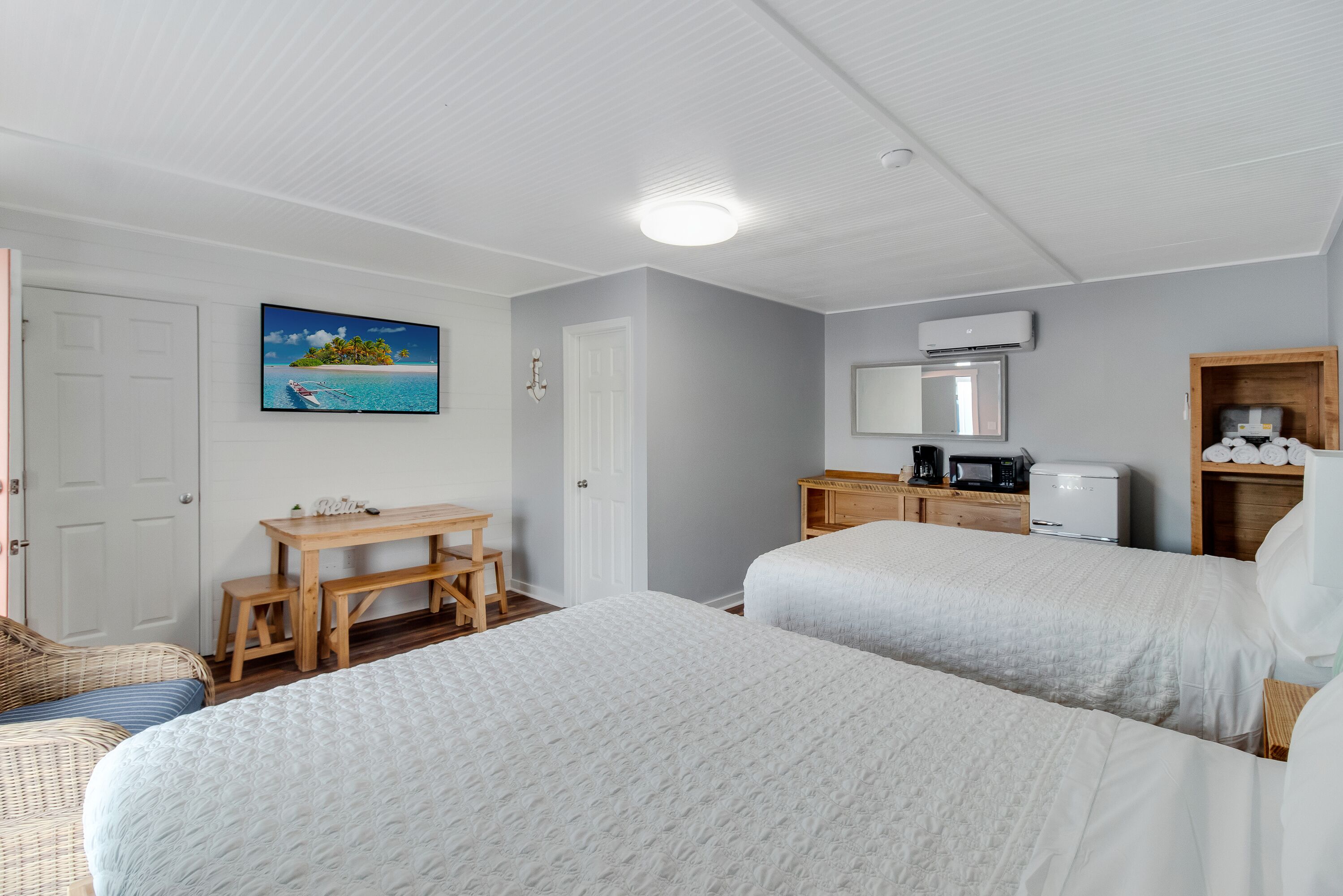 A hotel room with two beds, a wooden desk, a chair, a television, and a coffee maker.