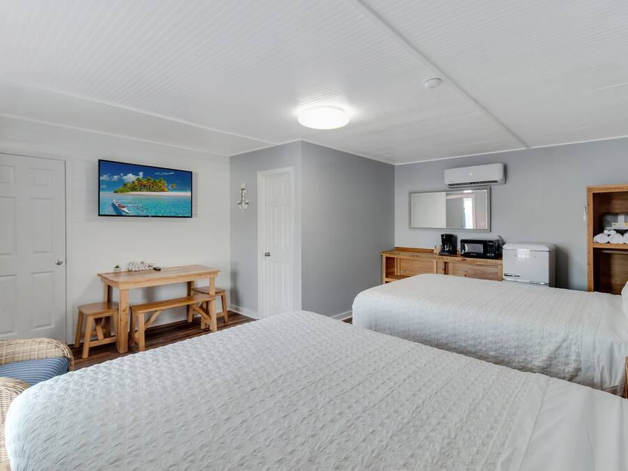 A hotel room with two beds, a wooden desk, a chair, a television, and a coffee maker.