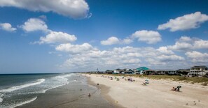 A beach with a clear sky, waves, and beachgoers. There are houses along the shore. - Anchor Inn Motel (Oak Island)