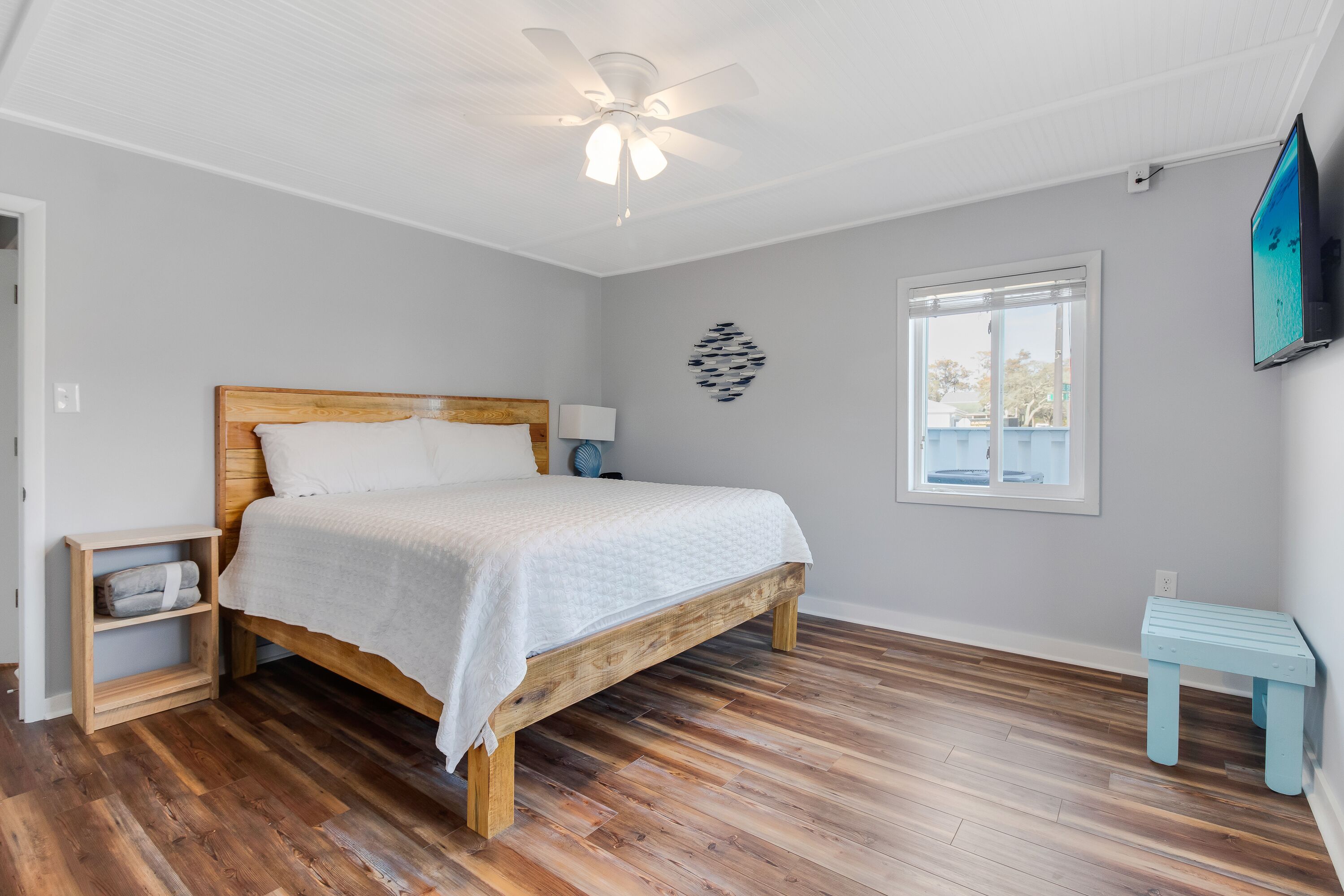 Un dormitorio con una cama de madera, ventilador de techo, televisor, ventana y una mesita.