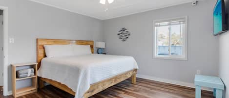 Un dormitorio con una cama de madera, ventilador de techo, televisor, ventana y una mesita.