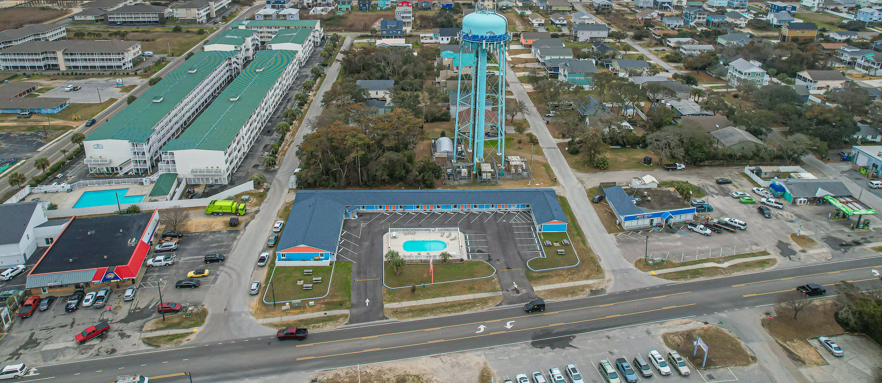An aerial view of a commercial area with a large parking lot, a swimming pool, and a tall water tower.