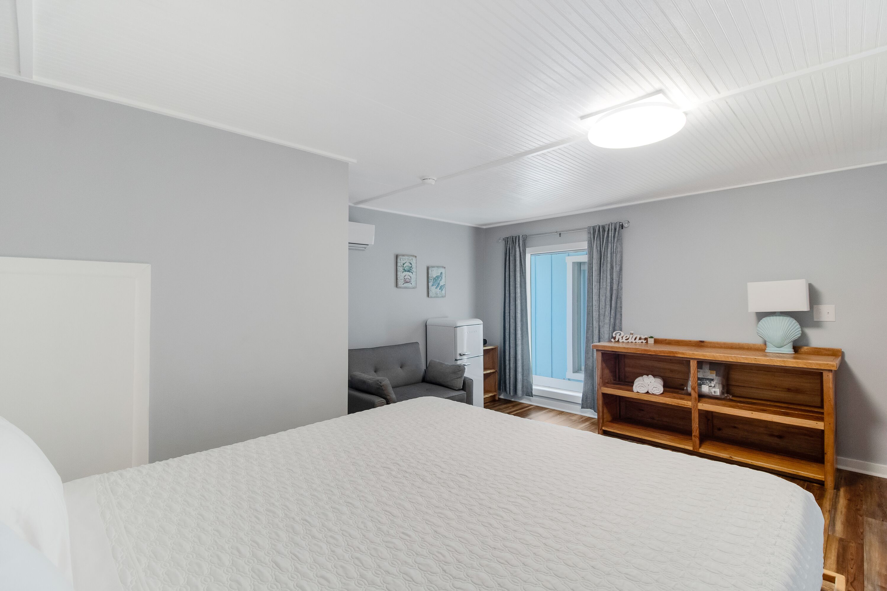 A bedroom with a large bed, a wooden nightstand, a desk, and a window with curtains.