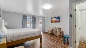 Quarto com cama de madeira, escrivaninha, cadeira e janela com cortinas.