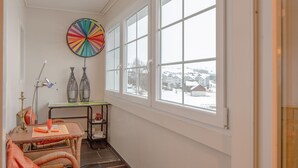 Ein gemütlicher Winkel mit Korbmöbeln, einer farbenfrohen Wanddekoration und Blick auf eine verschneite Landschaft durch große Fenster.