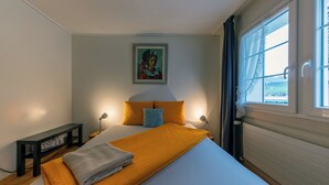 Ein ordentlich bezogenes Bett mit einer weißen und orangefarbenen Decke, zwei Kissen und einer Nachttischlampe.
