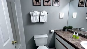 A bathroom with a toilet, two towels, a sink, and a mirror.