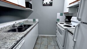 A compact kitchen with white cabinets, a granite countertop, a stove, and a refrigerator.