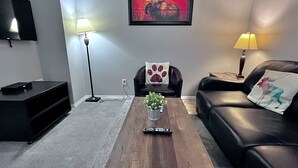 A living room with a wooden coffee table, a black leather sofa, a black TV stand, and a framed moose painting on the wall. - Two-Bedroom Apartment 131 - Private Entrance - Self Check In (BL-RES-12552) (Canmore)