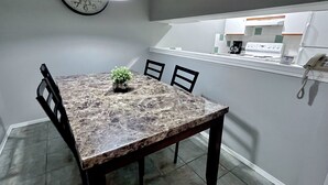 A dining area with a marble table, chairs, a clock, and a kitchen visible in the background. - Two-Bedroom Apartment 131 - Private Entrance - Self Check In (BL-RES-12552) (Canmore)