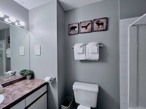 Um banheiro com parede cinza, vaso sanitário branco, pia com bancada de mármore, espelho com iluminação e três obras de arte com tema de animais.
