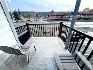 Ein Balkon mit zwei Holzstühlen, Blick auf einen Parkplatz und ein Gebäude mit rotem Dach im Hintergrund.