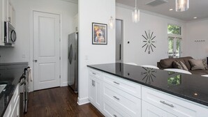 A modern kitchen with white cabinetry, a black countertop, and stainless steel appliances. There is a large island with a black countertop and a clock on the wall.