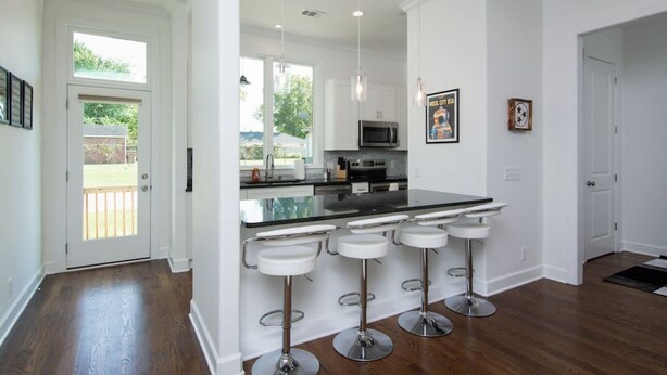 A modern kitchen with a central island, bar stools, pendant lighting, and a view of the outdoors.