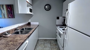 Eine kleine Küche mit weißen Schränken, einer Granit-Arbeitsplatte, einer Spüle, einem Herd und einem Kühlschrank.