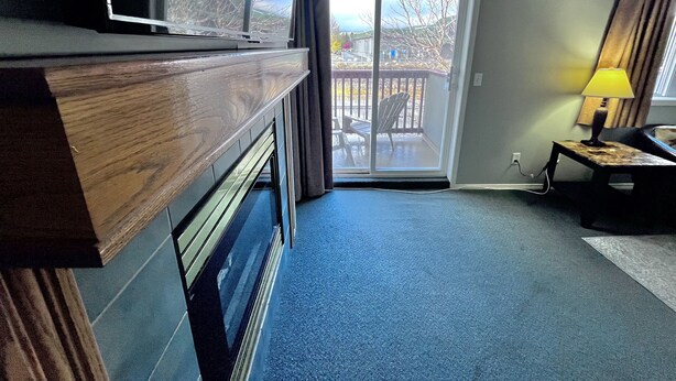 Ein Zimmer mit einer Schiebetür zum Balkon, einem kleinen Tisch mit einer Lampe und einem dunkelgrauen Sofa.