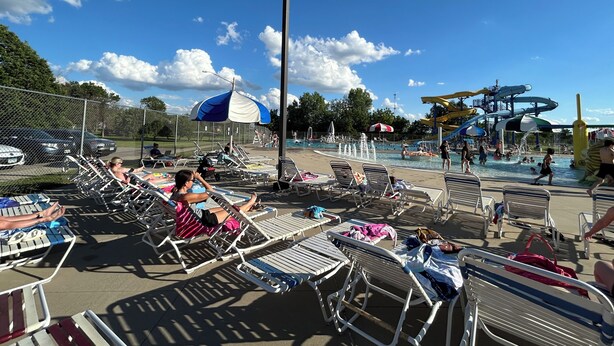 Zona de piscina amb gandules i ombrelles, tobogan aquàtic i aparcament tancat per tanca.