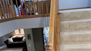 Una escala amb barana de fusta i graons amb moqueta que condueix a una zona d'aterratge amb un sofà i una cistella.