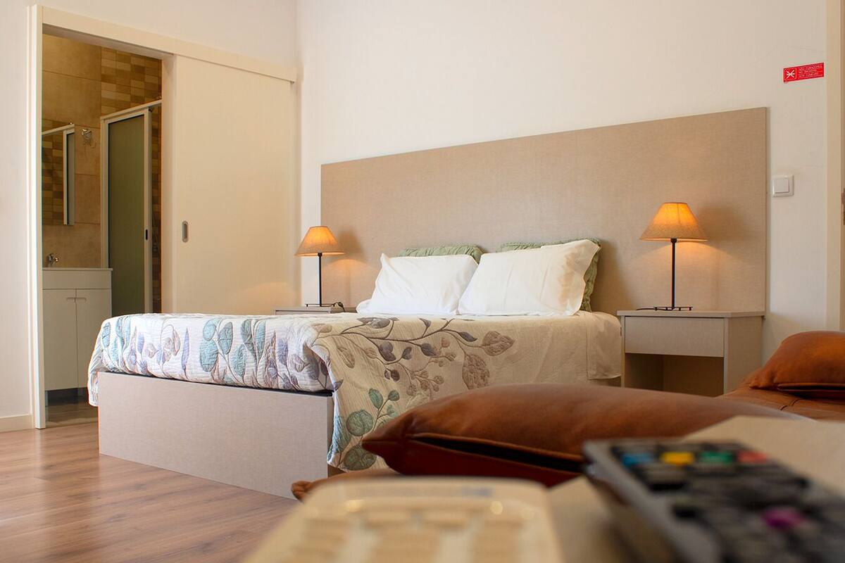 A hotel room with a bed, two bedside lamps, a nightstand, and a remote control on the floor.