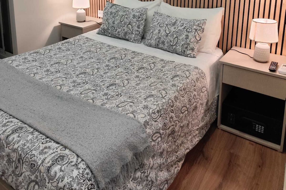 A neatly arranged hotel room with a bed, bedside tables, a lamp, and an air conditioning unit.