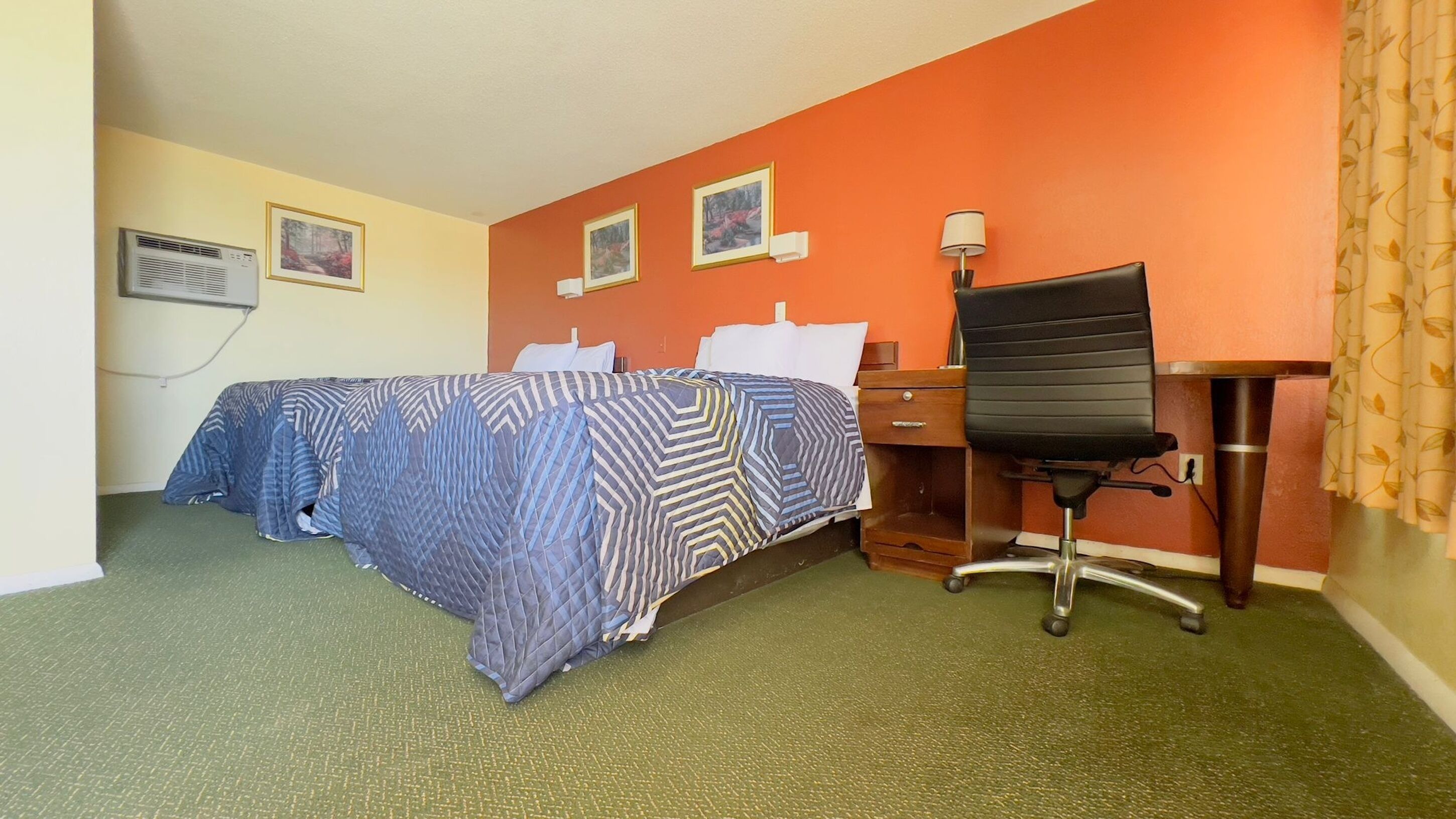 A hotel room with a bed, a desk, and a chair. There are three framed pictures on the wall.