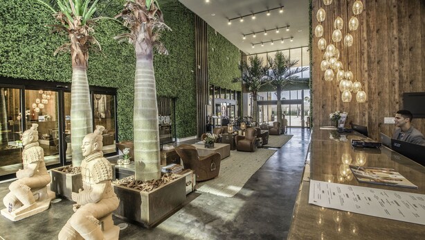 Un vestíbulo moderno con pared verde, zonas de estar y un mostrador de recepción.