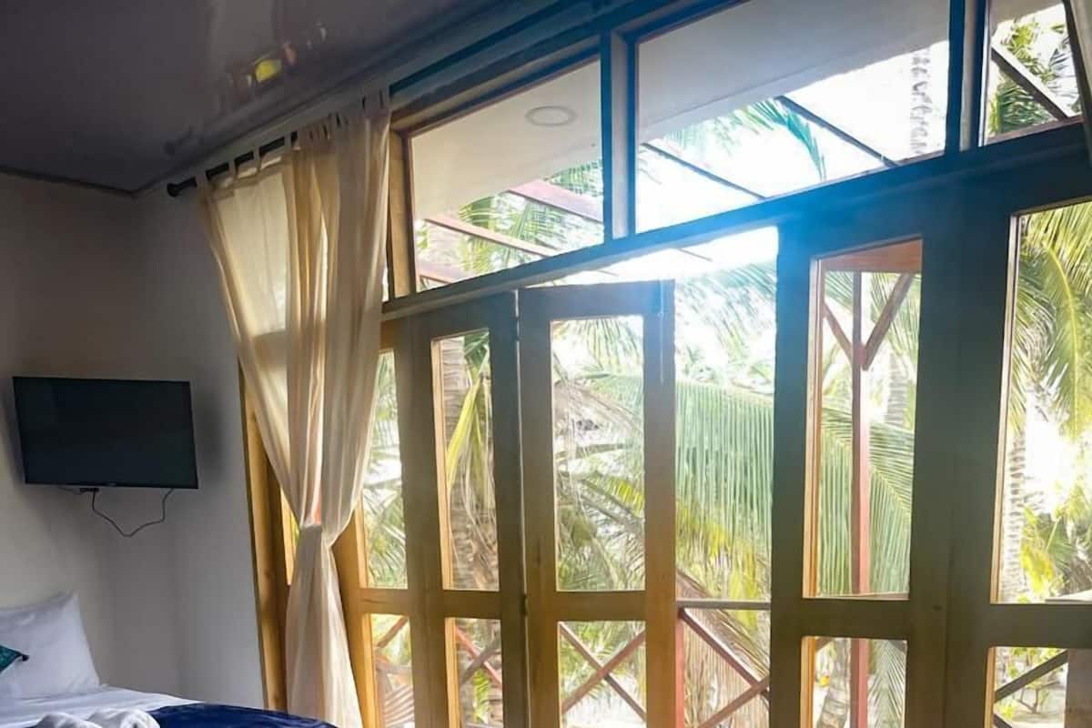 A hotel room with two beds, a TV, and large windows with curtains.