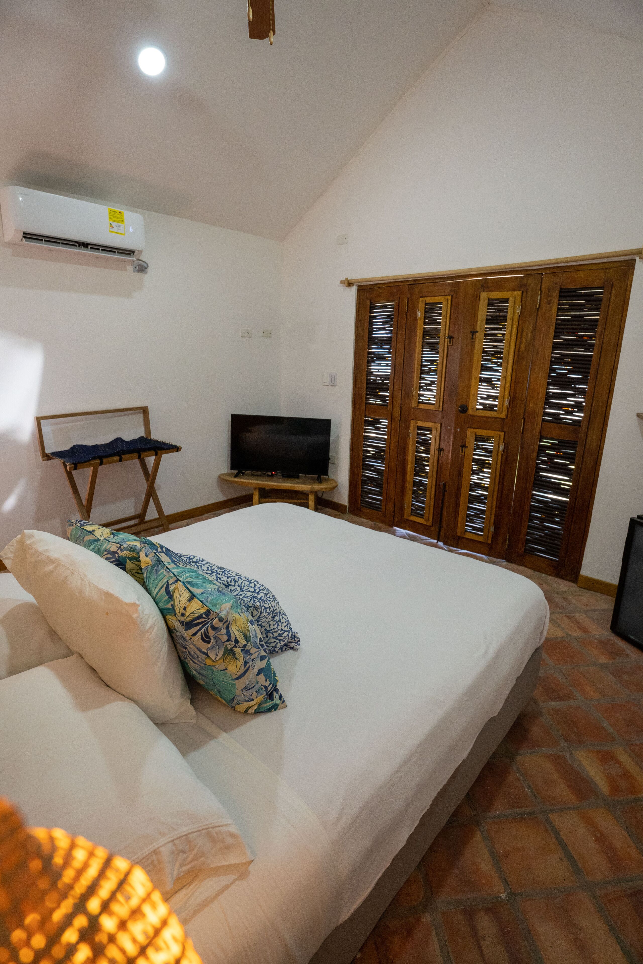A bedroom with a bed, a television, an air conditioning unit, and a wardrobe with glass doors.