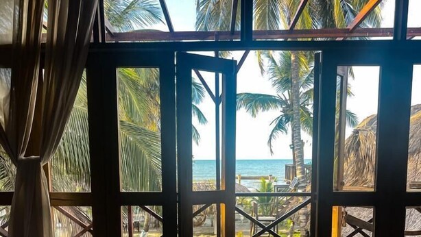 A room with a view of the beach, featuring two beds, a large glass door, and a concrete floor. - CASA ORIGEN BOUTIQUE (San Bernardo del Viento)